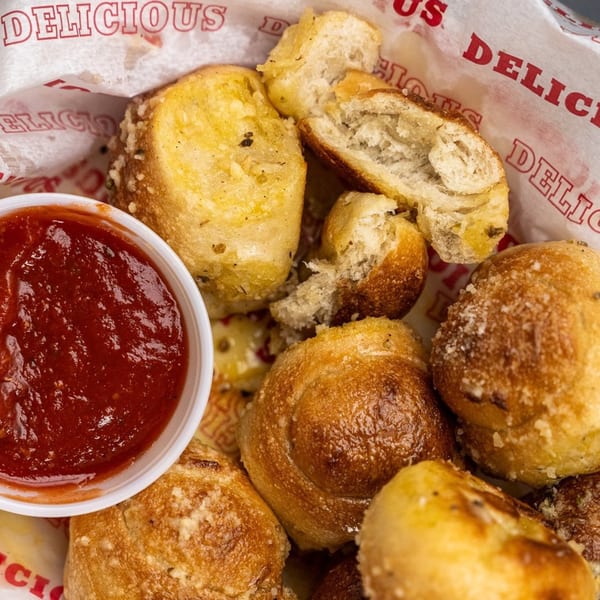 Five Star Pizza garlic knots with marinara sauce in a paper-lined basket.