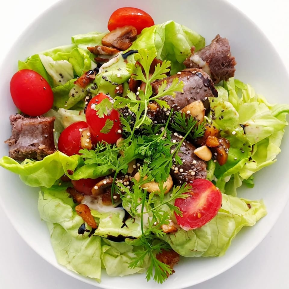 Fresh green salad with cherry tomatoes, meat, nuts, and seeds in a white bowl.