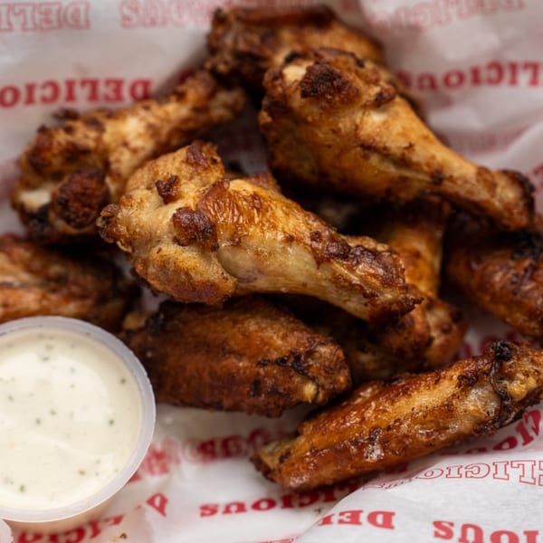 Crispy, golden-brown chicken wings in a paper-lined basket with a side of ranch dressing.